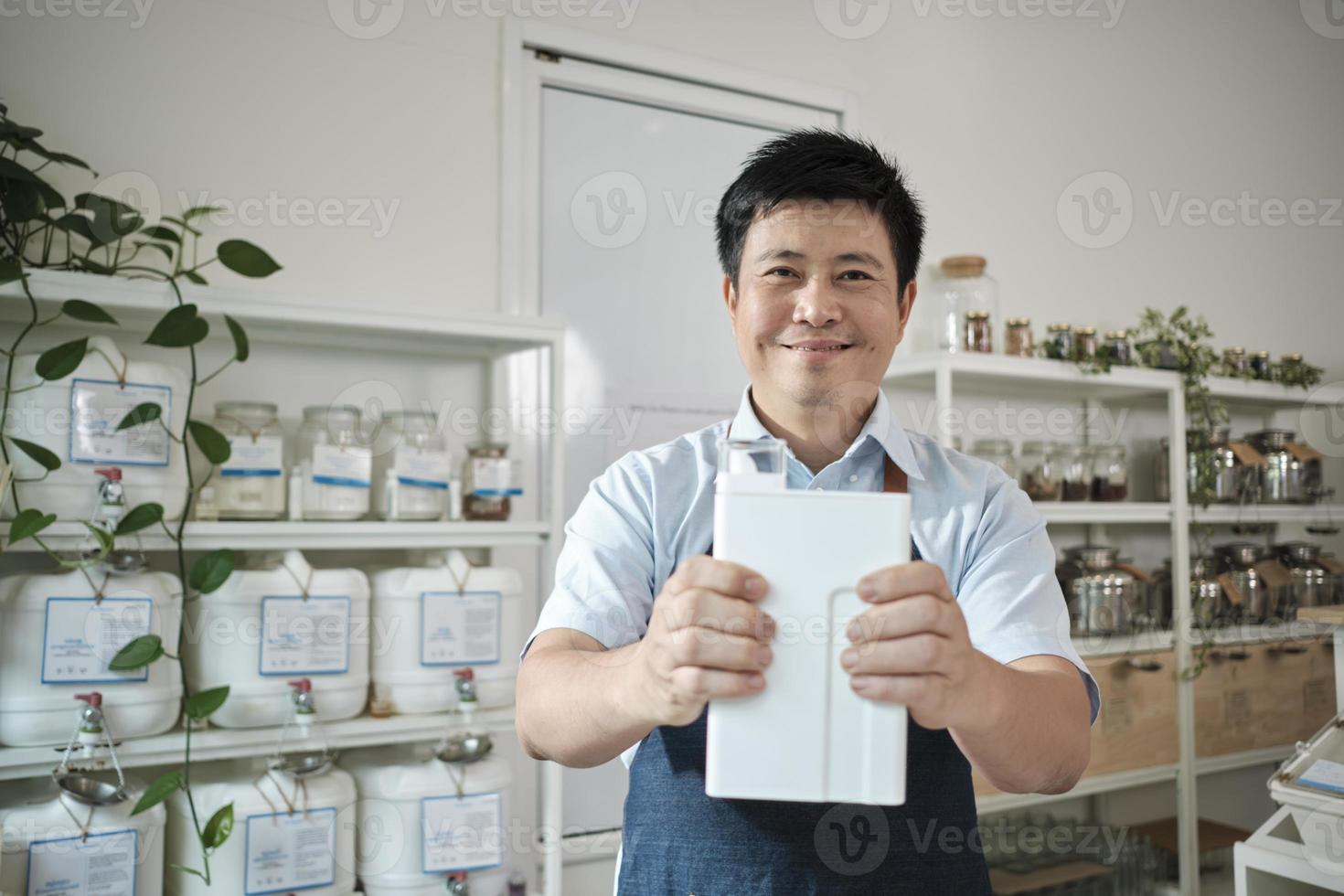 Portrait of Thai male shopkeeper smiles and looks at camera with reusable container, organic products at refill store, zero-waste grocery, and plastic-free, environment-friendly sustainable business. photo