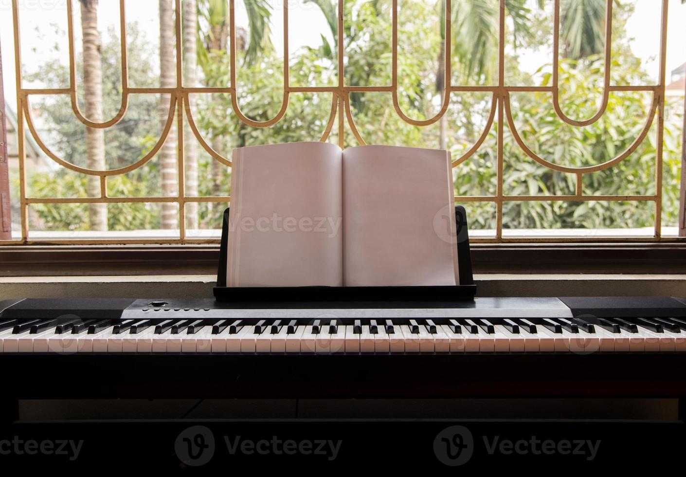 Electric piano with empty sheet music near the big window overlooking green garden, front view photo