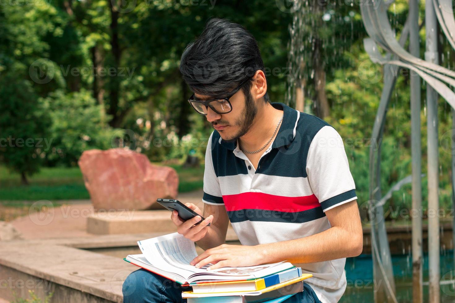 Young brunette student boy with books in hands using a mobile phone photo