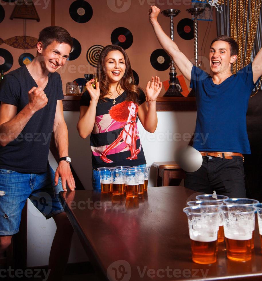 Twins playing beerpong with beautiful brunette in bar photo