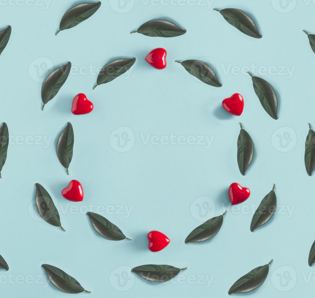 Creative circle arrangemen with red hearts and  green leaves on a blue background. Valentines day and spring concept with copy space. Flat lay. Minimal nature. photo