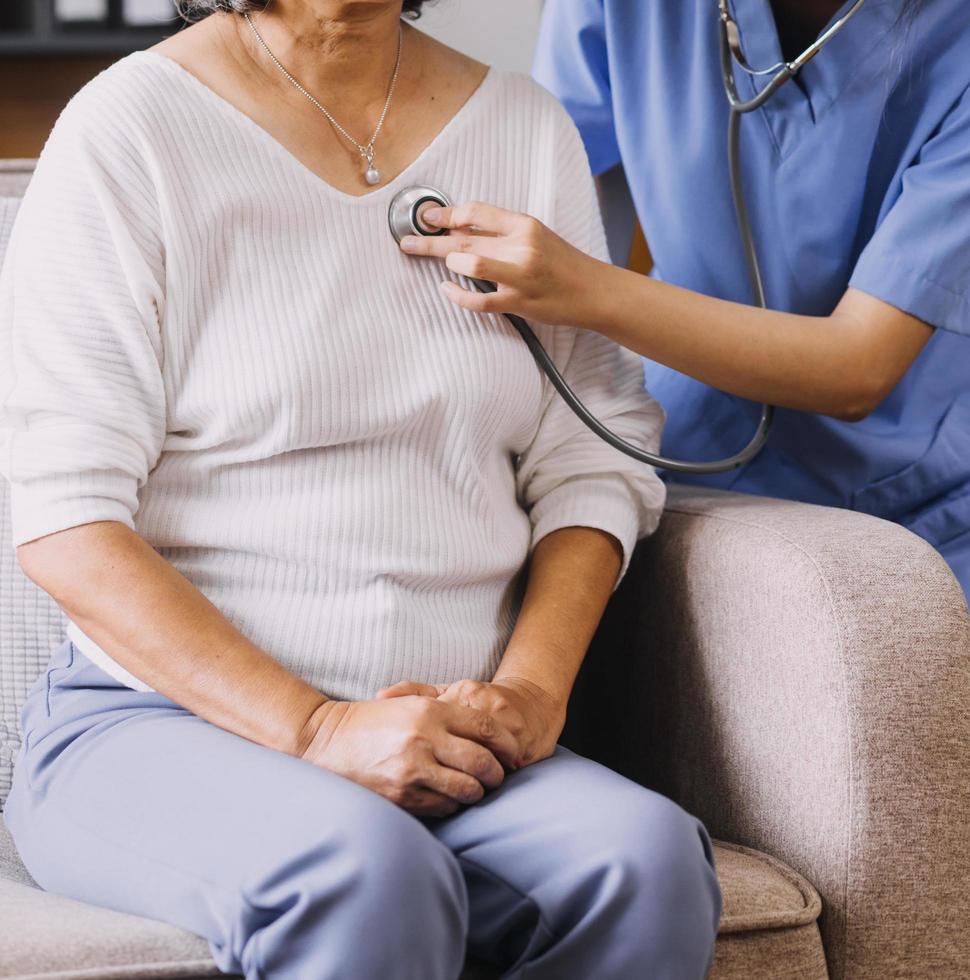 Homecare nursing service and elderly people cardiology healthcare. Close up of young hispanic female doctor nurse check mature caucasian man patient heartbeat using stethoscope during visit photo