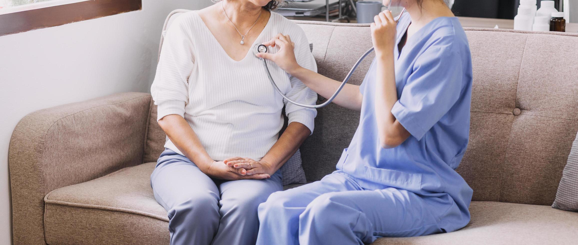 Homecare nursing service and elderly people cardiology healthcare. Close up of young hispanic female doctor nurse check mature caucasian man patient heartbeat using stethoscope during visit photo