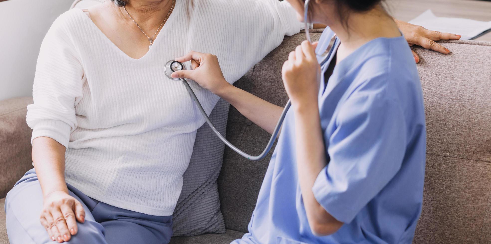 Homecare nursing service and elderly people cardiology healthcare. Close up of young hispanic female doctor nurse check mature caucasian man patient heartbeat using stethoscope during visit photo