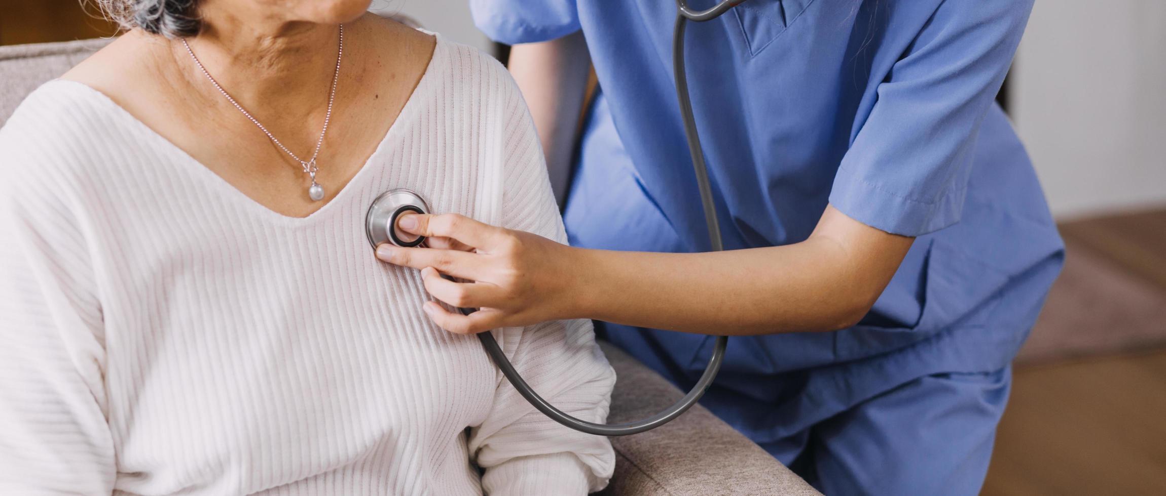 Homecare nursing service and elderly people cardiology healthcare. Close up of young hispanic female doctor nurse check mature caucasian man patient heartbeat using stethoscope during visit photo