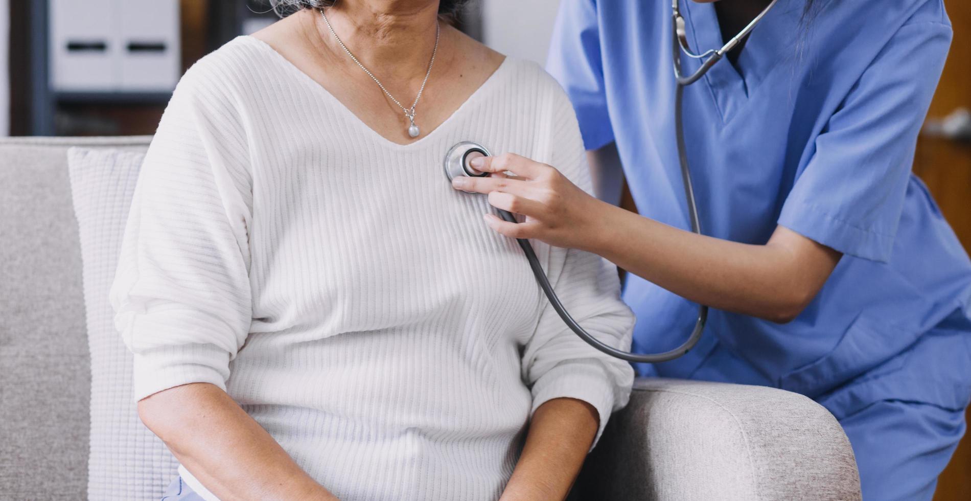 Homecare nursing service and elderly people cardiology healthcare. Close up of young hispanic female doctor nurse check mature caucasian man patient heartbeat using stethoscope during visit photo