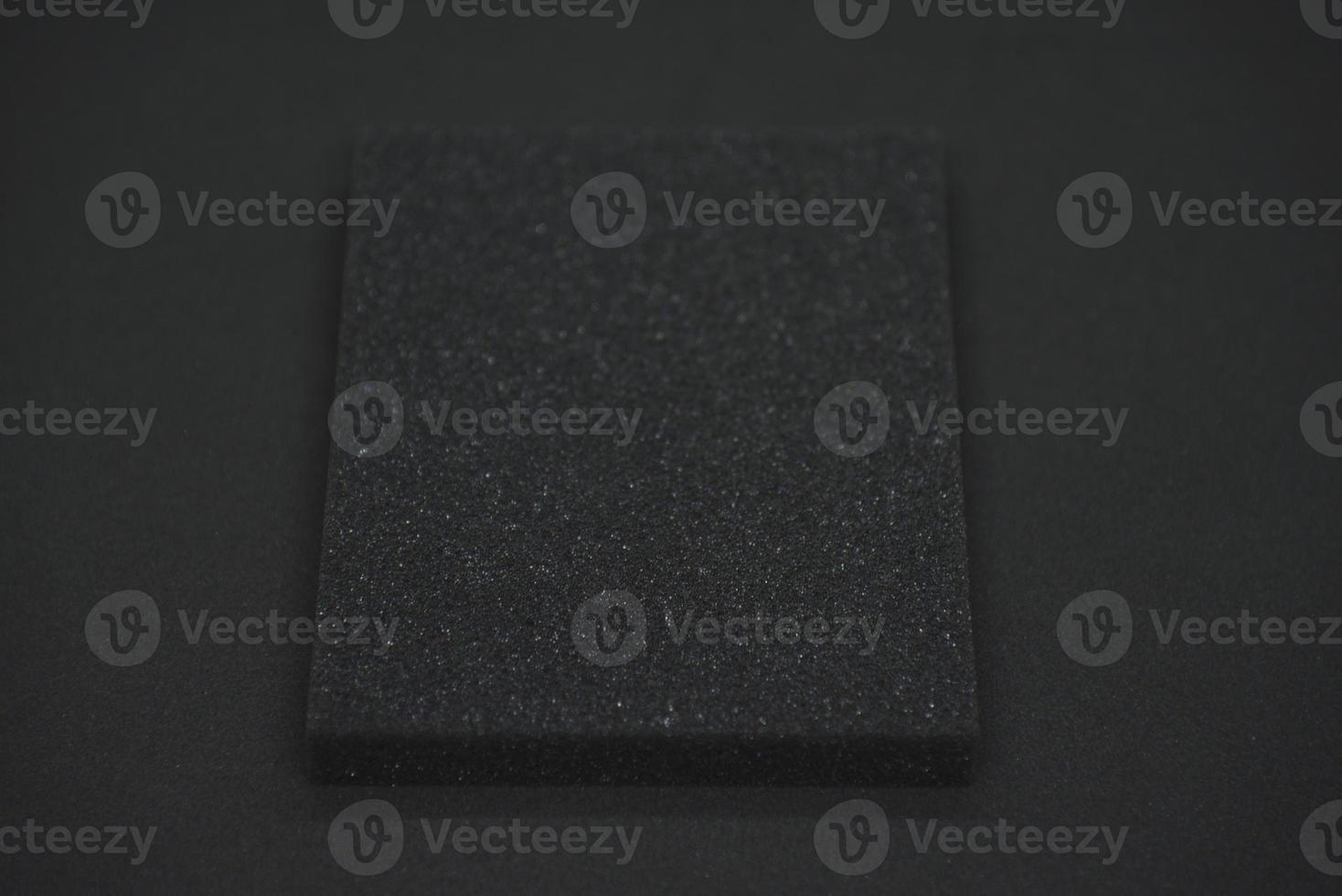 A black sponge on a black background. Black foam rubber on black cloth. The black square of the gasket. photo