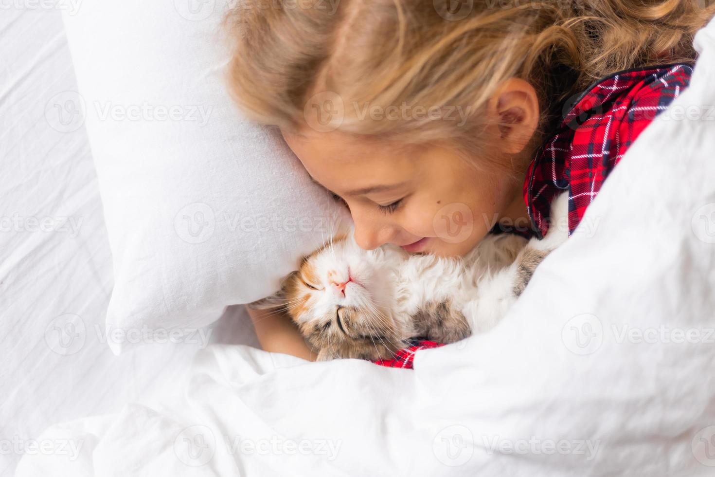 a cute little girl is sleeping sweetly at home in a rabbit with a kitten. White cotton bed linen. Christmas holidays. Children and pets at home photo