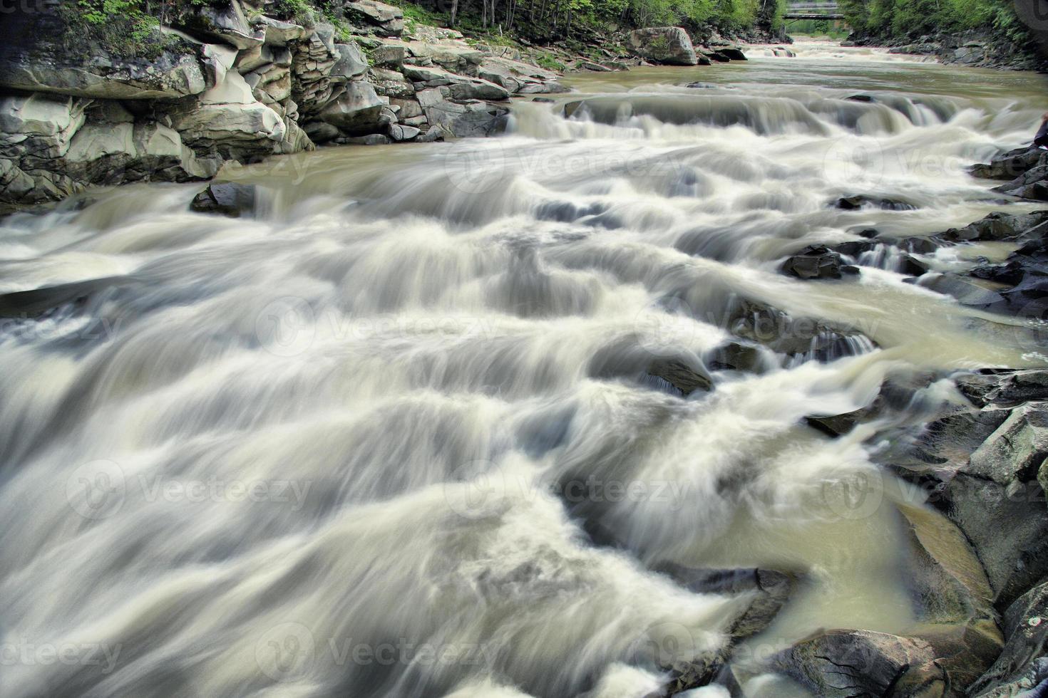un río de montaña fluye lentamente sobre las piedras como una pequeña cascada. foto