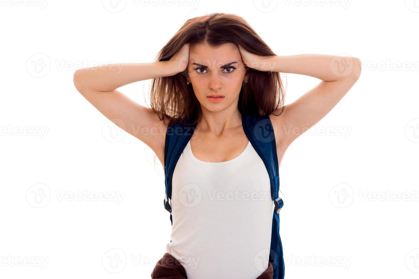 anfry smart student girl in brown sport clothes with backpack on her shoulders looking at the camera with hands on her head isolated on white background photo