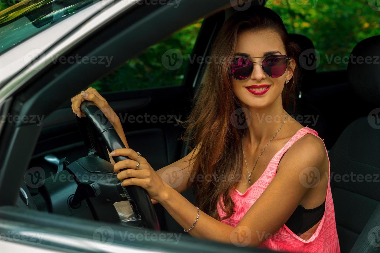 retrato de una joven morena glamorosa con gafas mientras conduce en el auto foto