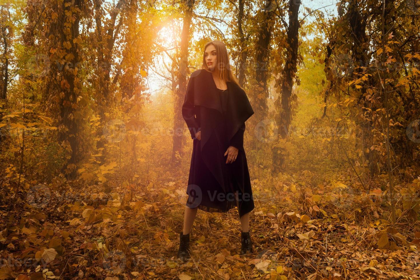 joven rubia con abrigo negro mirando hacia otro lado en el bosque dorado de otoño foto