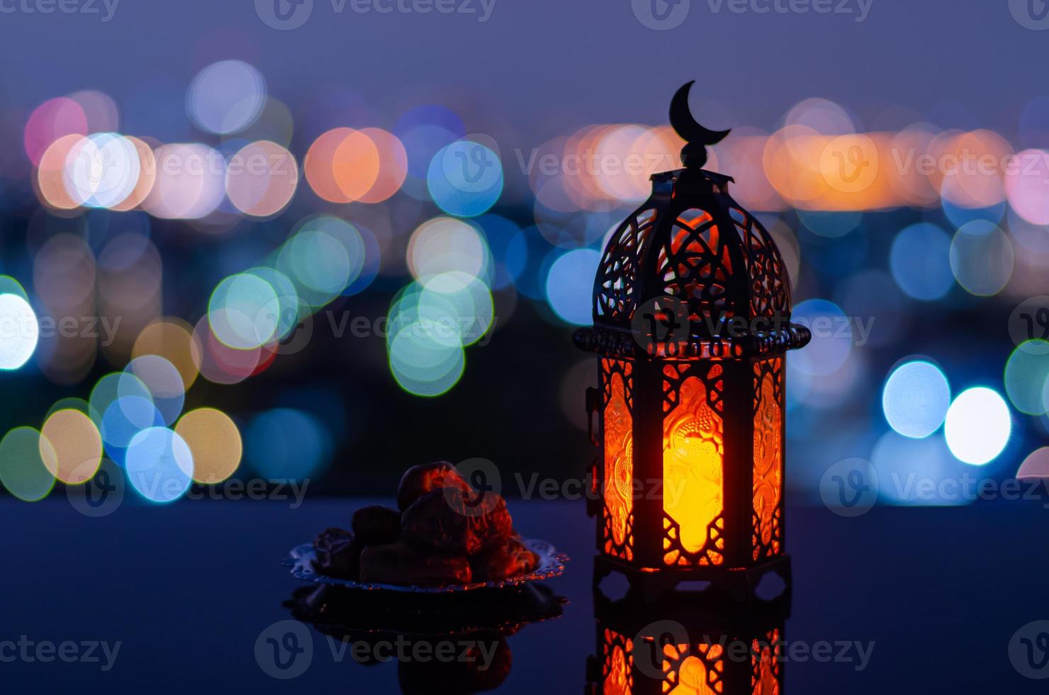 Selective focus of lantern that have moon symbol on top and small plate of dates fruit with city bokeh light background for the Muslim feast of the holy month of Ramadan Kareem. photo