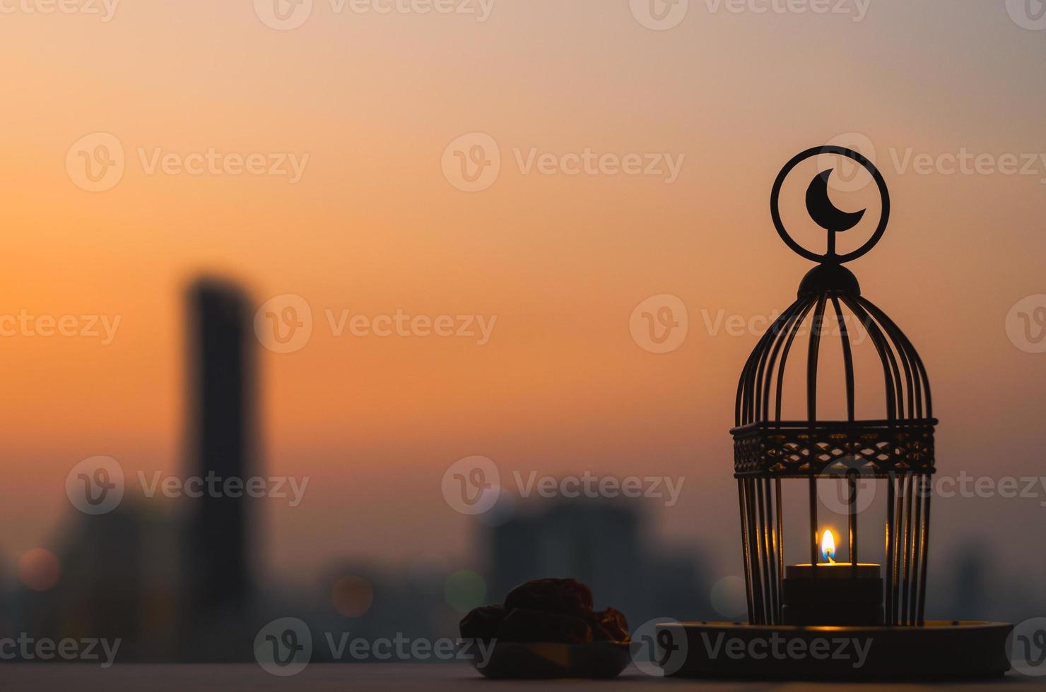 Lantern that have moon symbol on top and small plate of dates fruit with dusk sky and city background for the Muslim feast of the holy month of Ramadan Kareem. photo