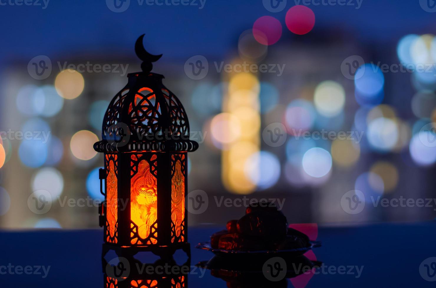Selective focus of lantern and small plate of dates fruit with apartment building background for the Muslim feast of the holy month of Ramadan Kareem. photo