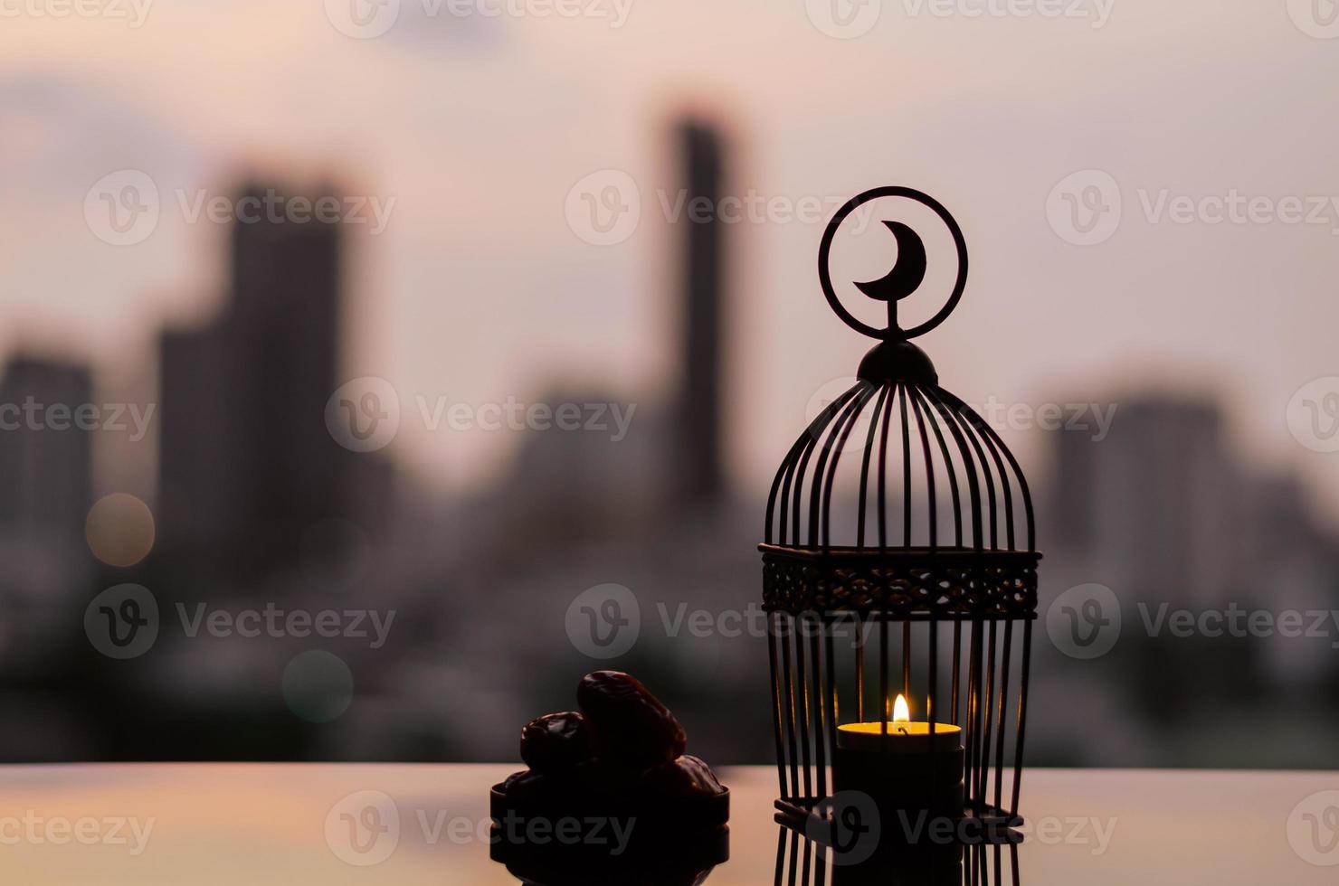 linterna que tiene el símbolo de la luna en la parte superior y un pequeño plato de fruta de dátiles con el cielo del amanecer y el fondo de la ciudad para la fiesta musulmana del mes sagrado del ramadán kareem. foto