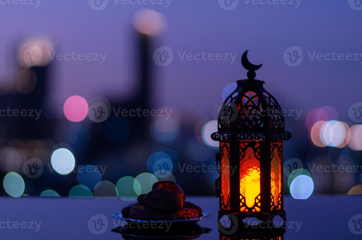 Selective focus of lantern that have moon symbol on top and small plate of dates fruit with city bokeh light background for the Muslim feast of the holy month of Ramadan Kareem. photo