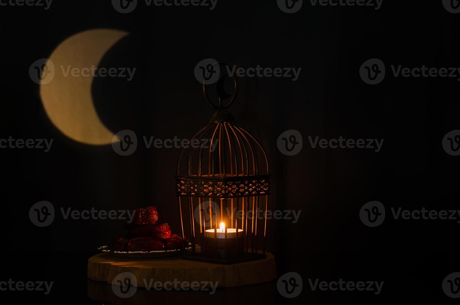 Lantern and small plate of dates fruit on wooden tray with moon shape from light on background for the Muslim feast of the holy month of Ramadan Kareem. photo