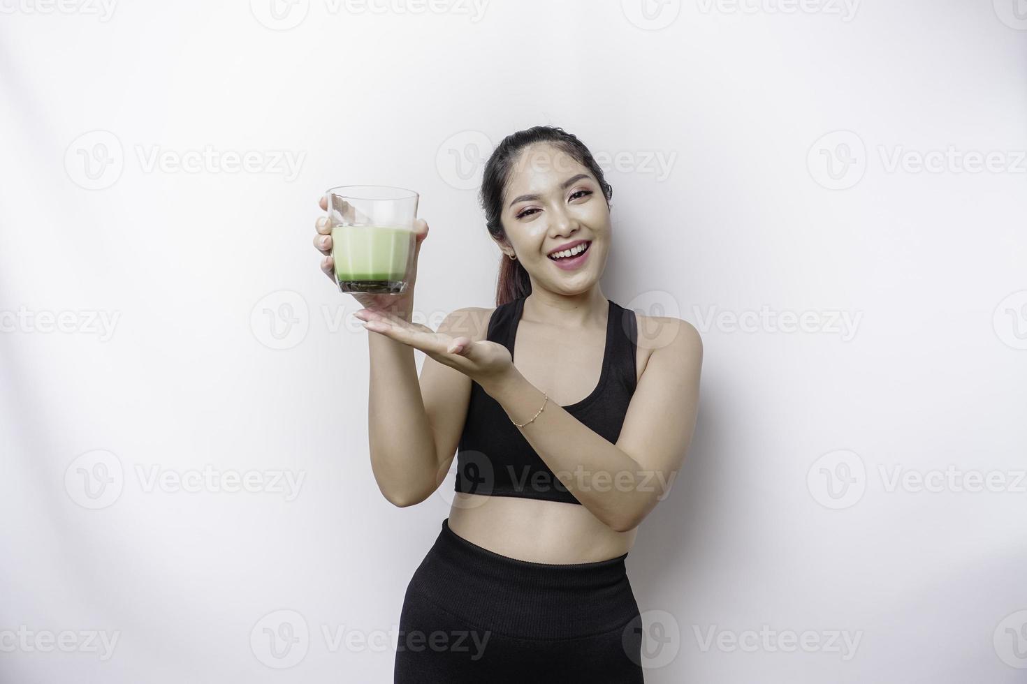 alegre mujer asiática deportiva que usa ropa deportiva con un vaso de sabroso batido verde, aislada de fondo blanco. foto