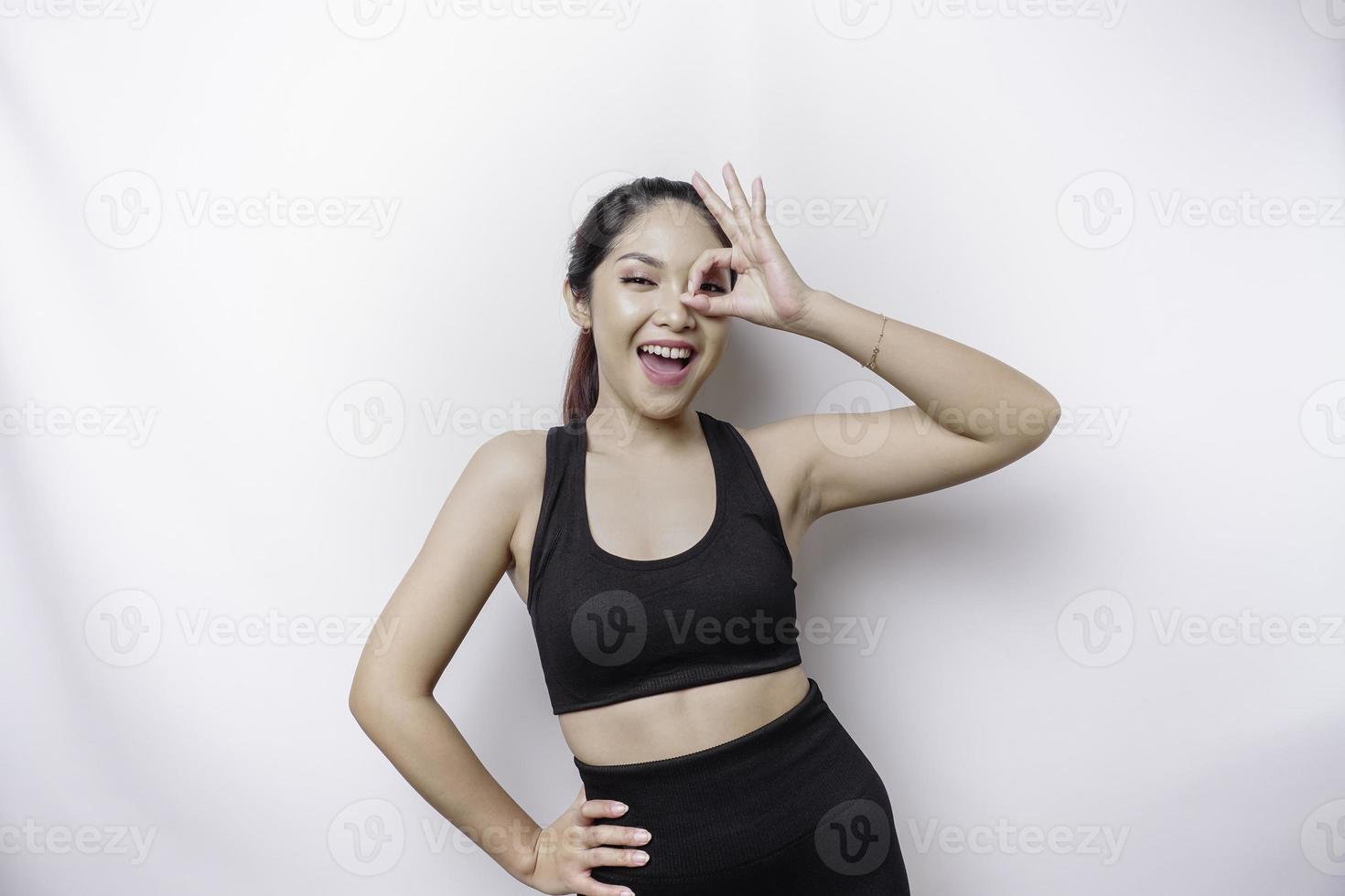 Excited sporty Asian woman wearing a sportswear is giving an OK hand gesture isolated by a white background photo