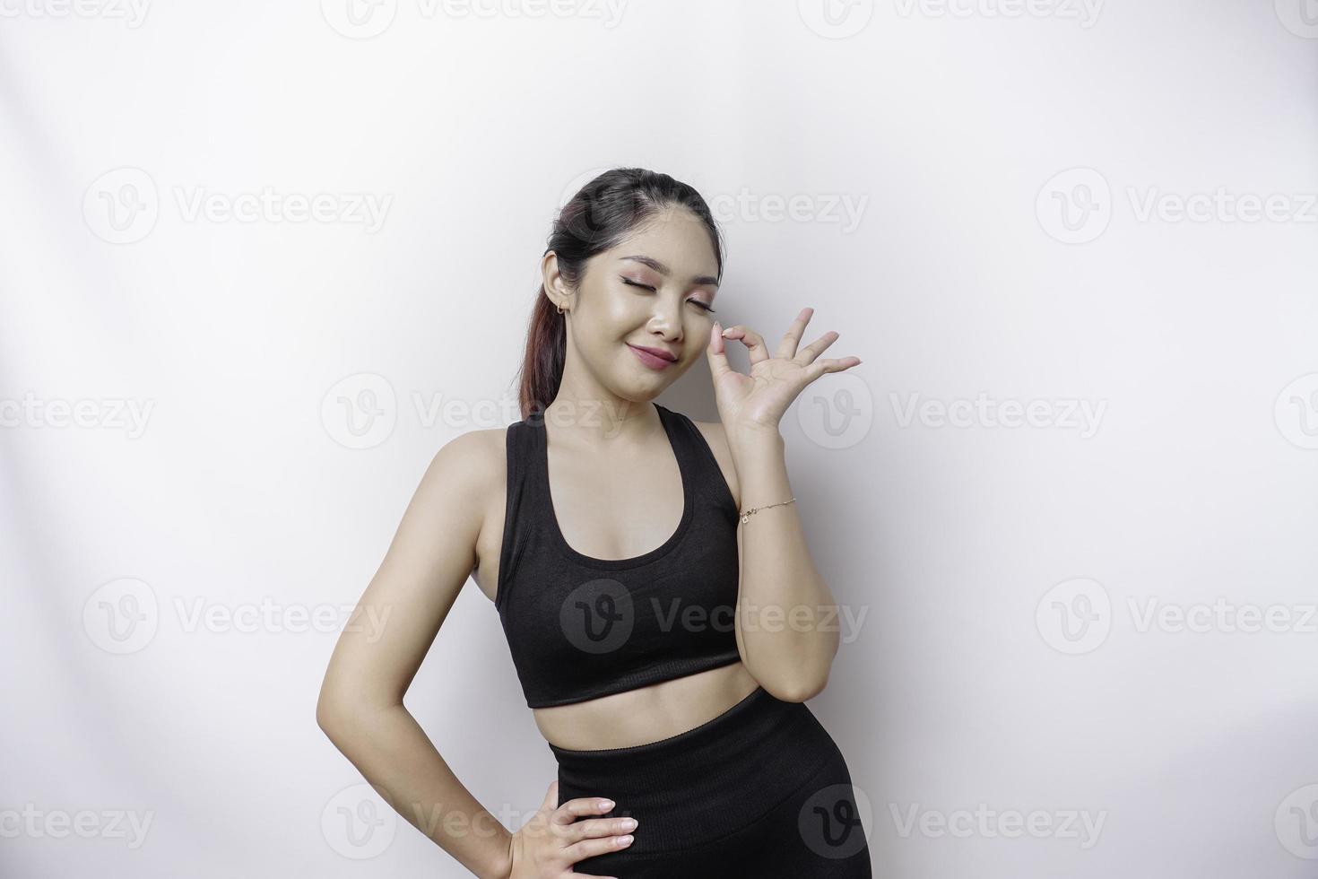 Excited sporty Asian woman wearing a sportswear is giving an OK hand gesture isolated by a white background photo