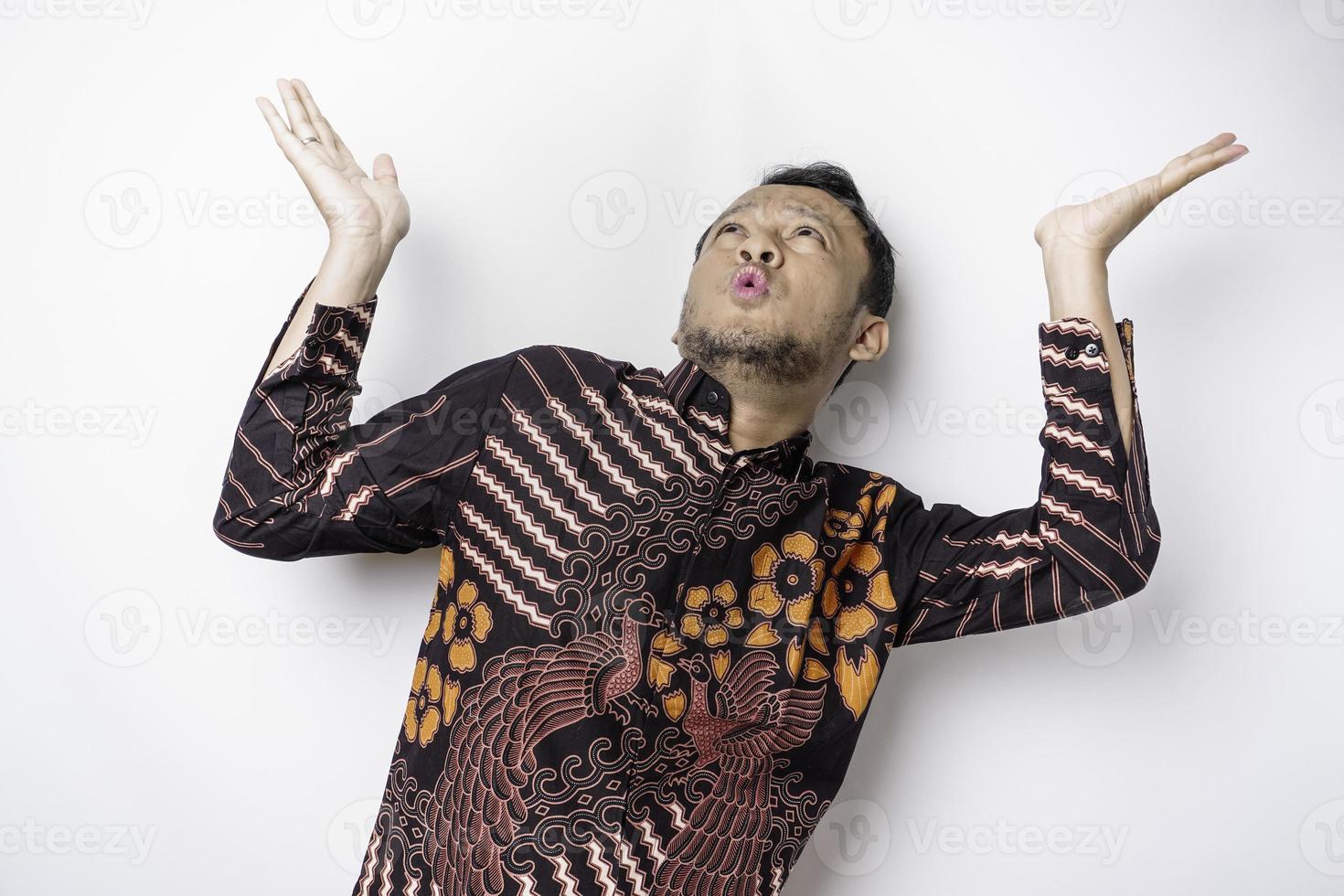 Shocked Asian man wearing batik shirt pointing at the copy space on top of him, isolated by white background photo
