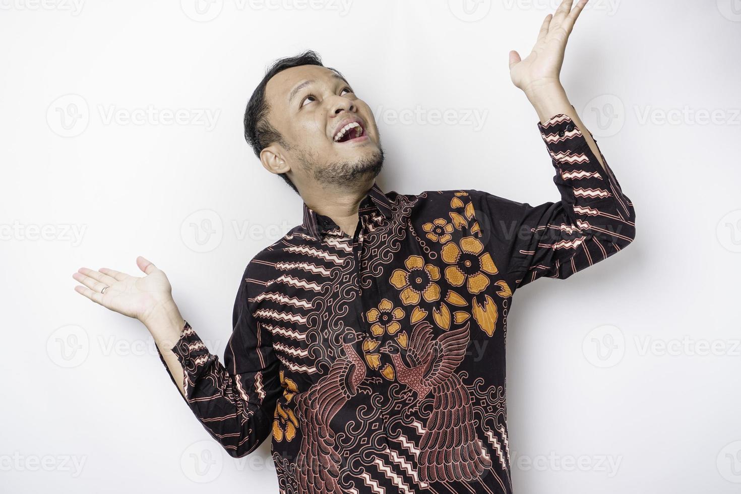 emocionado hombre asiático con pantalones batik apuntando al espacio de copia encima de él, aislado por fondo blanco foto