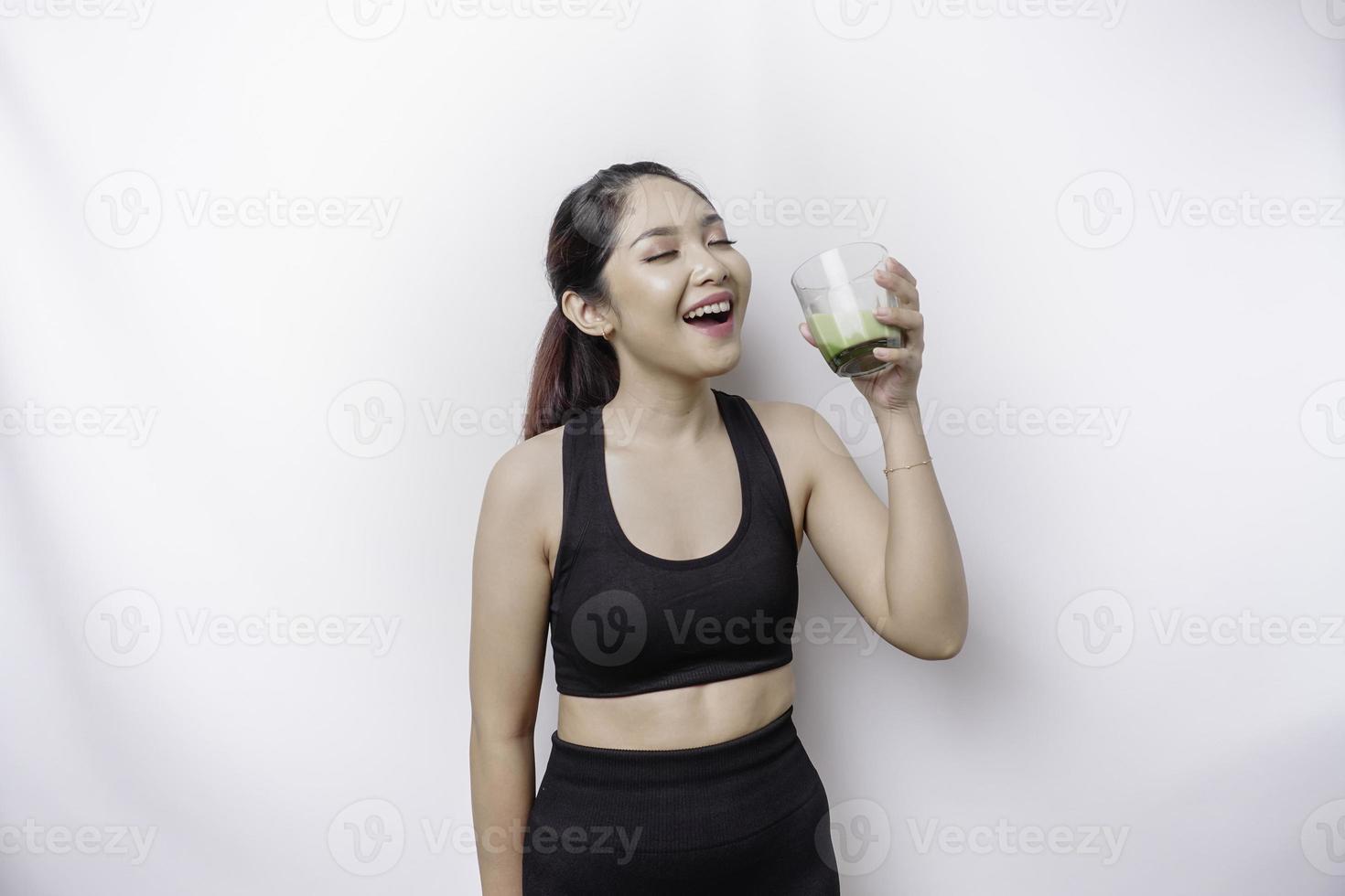 alegre mujer asiática deportiva que usa ropa deportiva con un vaso de sabroso batido verde, aislada de fondo blanco. foto