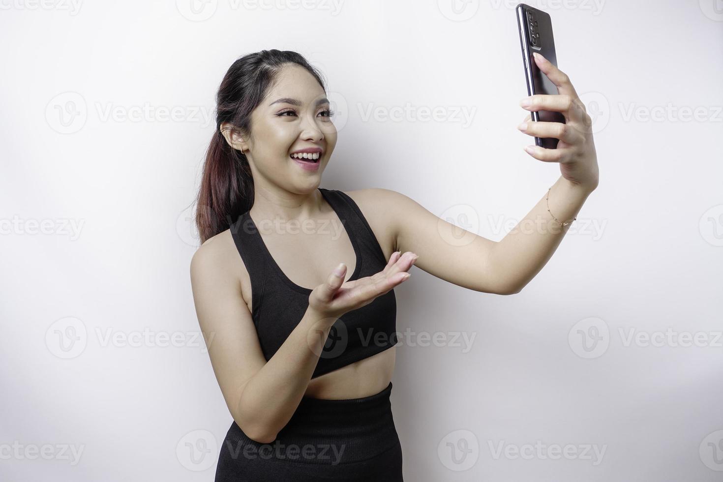 A portrait of a sporty Asian woman wearing a sportswear and holding her phone, isolated by white background photo