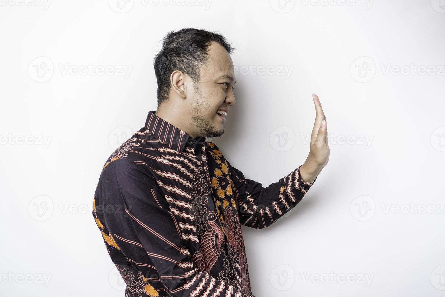 emocionado hombre asiático con pantalones batik apuntando al espacio de copia a su lado, aislado por fondo blanco foto
