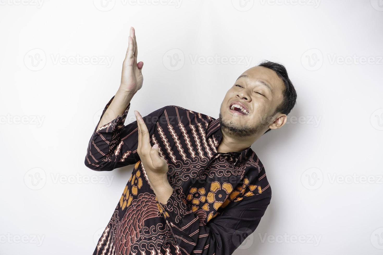 emocionado hombre asiático con pantalones batik apuntando al espacio de copia encima de él, aislado por fondo blanco foto