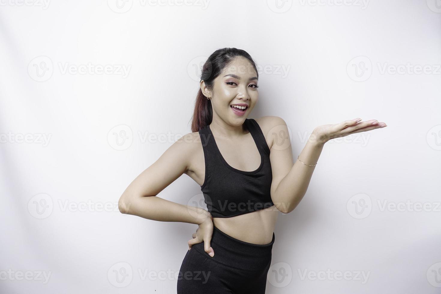 Excited Asian sporty woman wearing sportwear pointing at the copy space beside her, isolated by white background photo