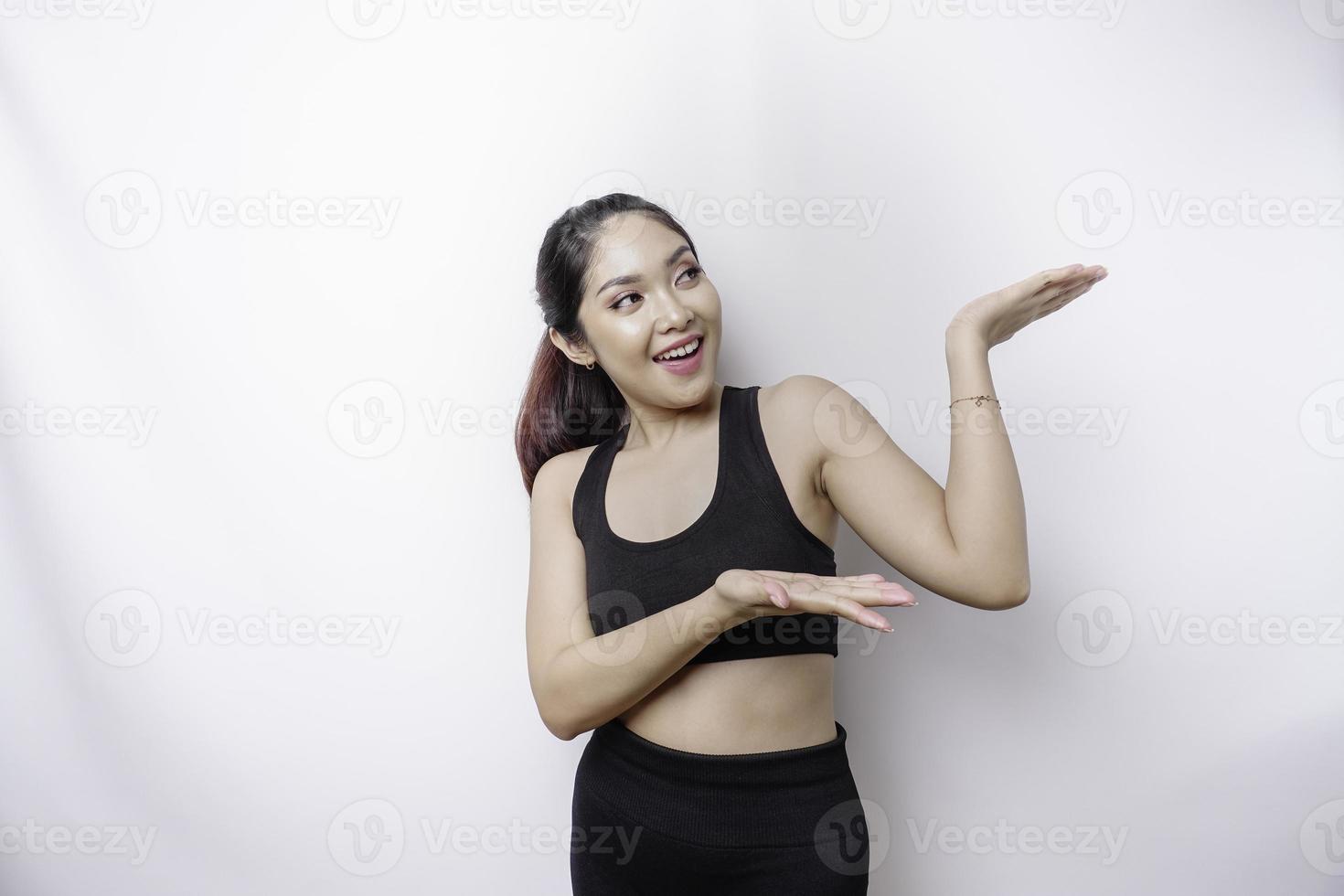 Excited Asian sporty woman wearing sportswear pointing at the copy space on top of her, isolated by white background photo
