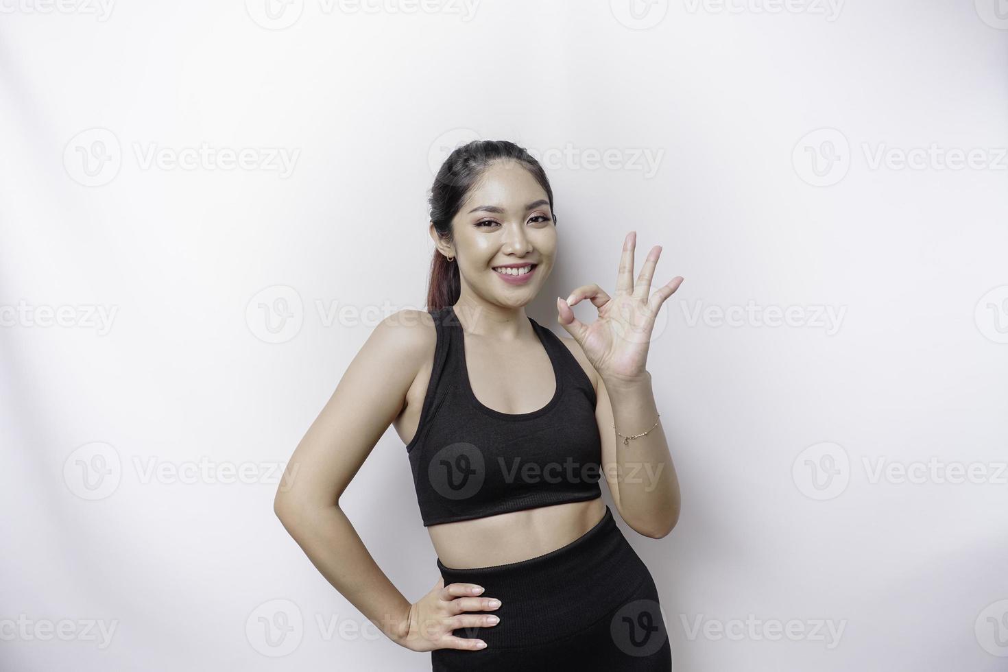 Excited sporty Asian woman wearing a sportswear is giving an OK hand gesture isolated by a white background photo