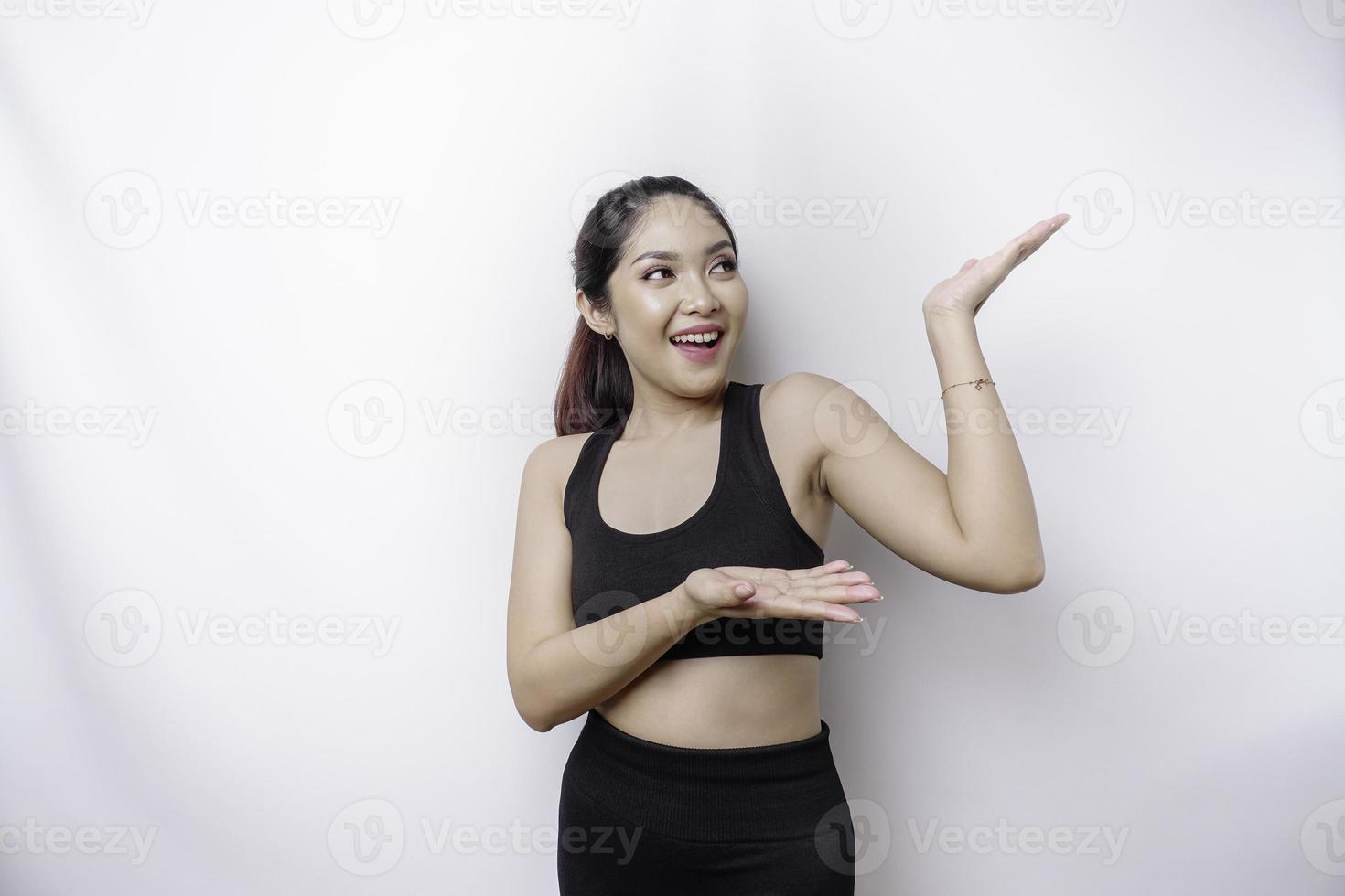 Excited Asian sporty woman wearing sportswear pointing at the copy space on top of her, isolated by white background photo
