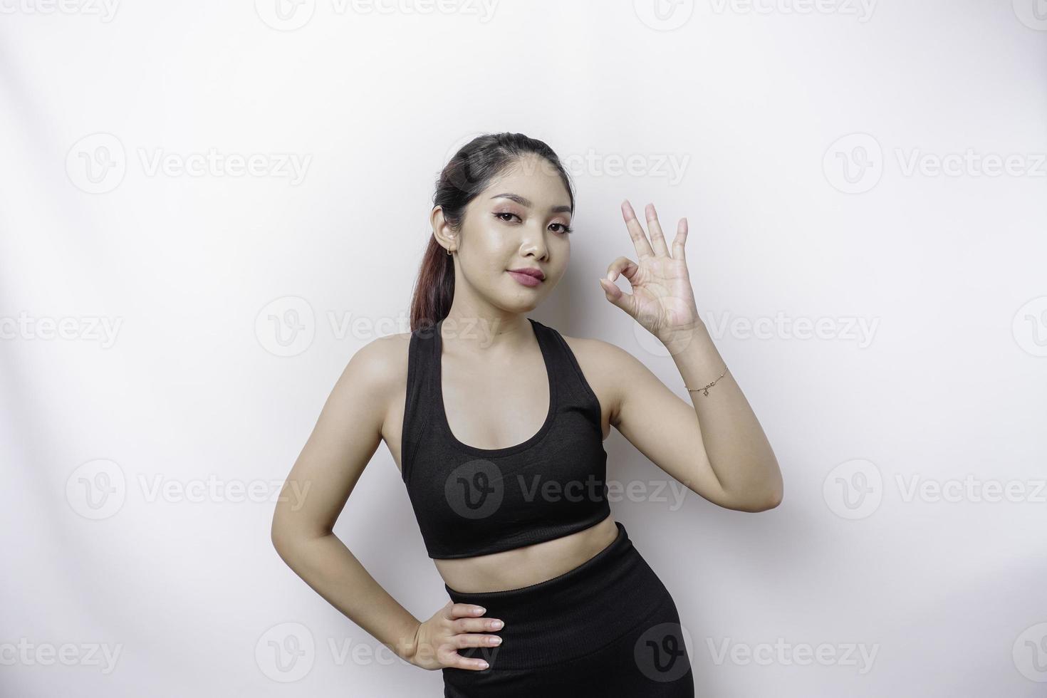 Excited sporty Asian woman wearing a sportswear is giving an OK hand gesture isolated by a white background photo