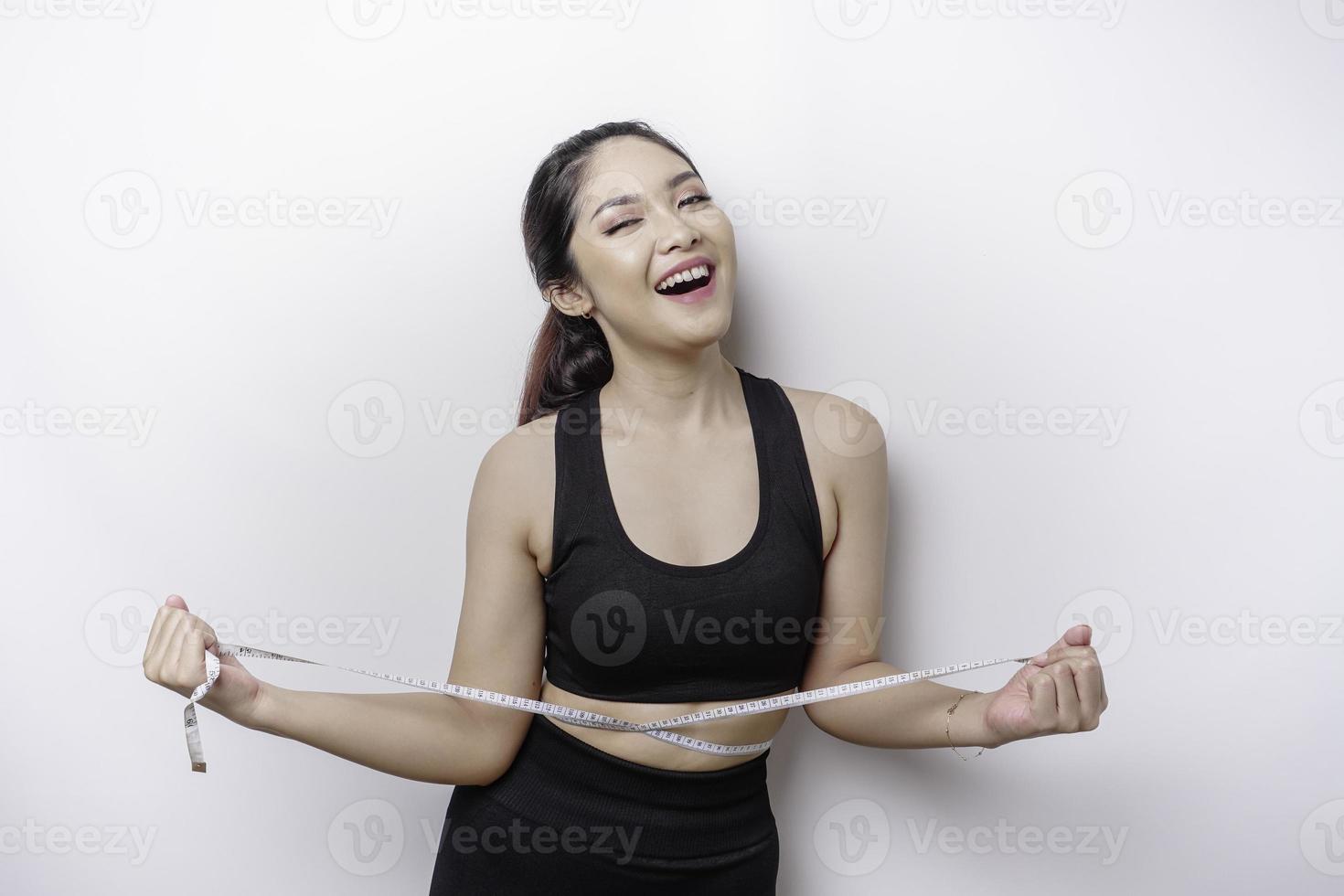 Portrait of cheerful young Asian woman in sportswear measuring waist with tape, feeling happy about losing weight at home. Healthy lifestyle, sports and slimming diet concept photo