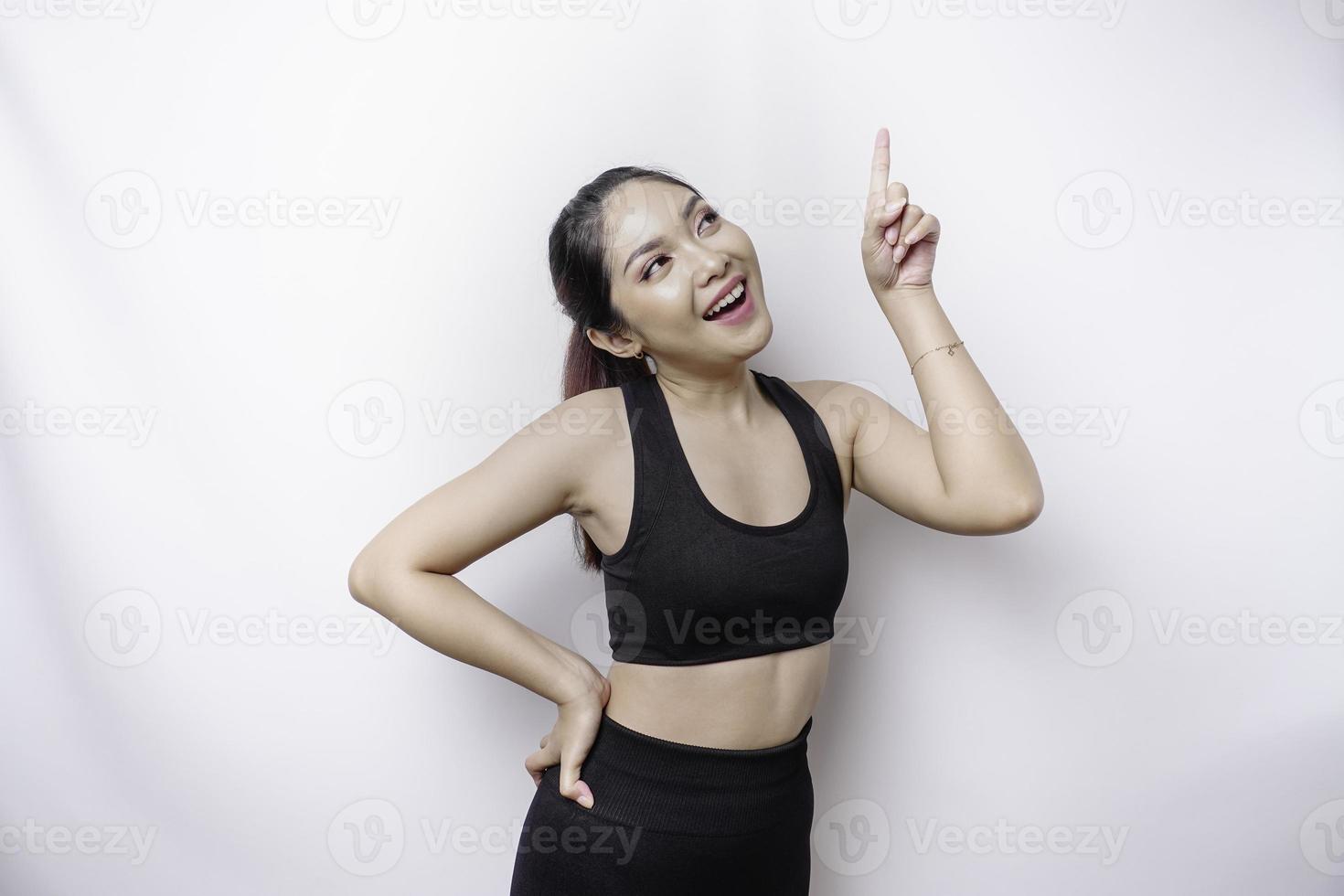 Excited Asian sporty woman wearing sportswear pointing at the copy space on top of her, isolated by white background photo