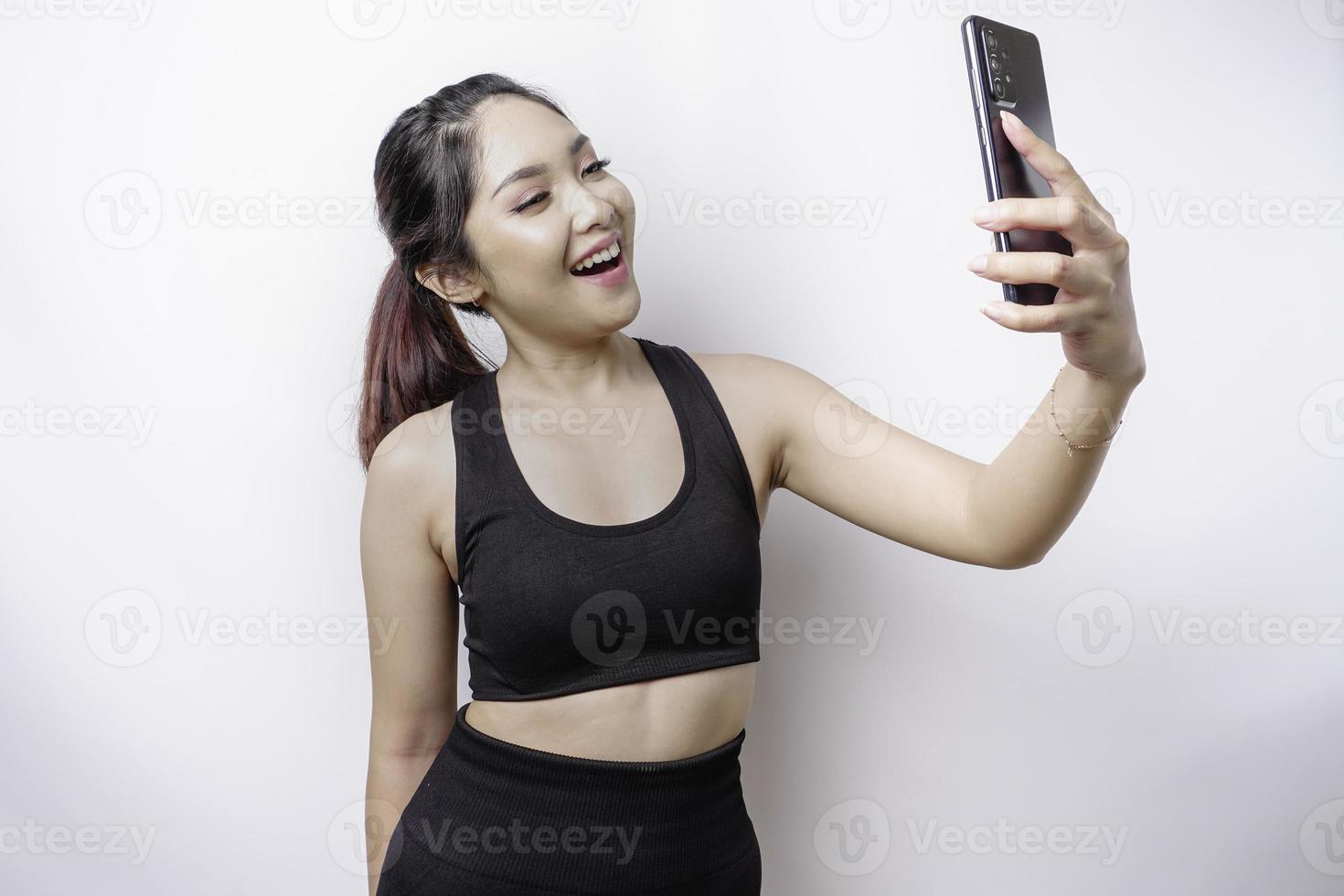 un retrato de una mujer asiática deportiva que usa ropa deportiva y sostiene su teléfono, aislada de fondo blanco foto