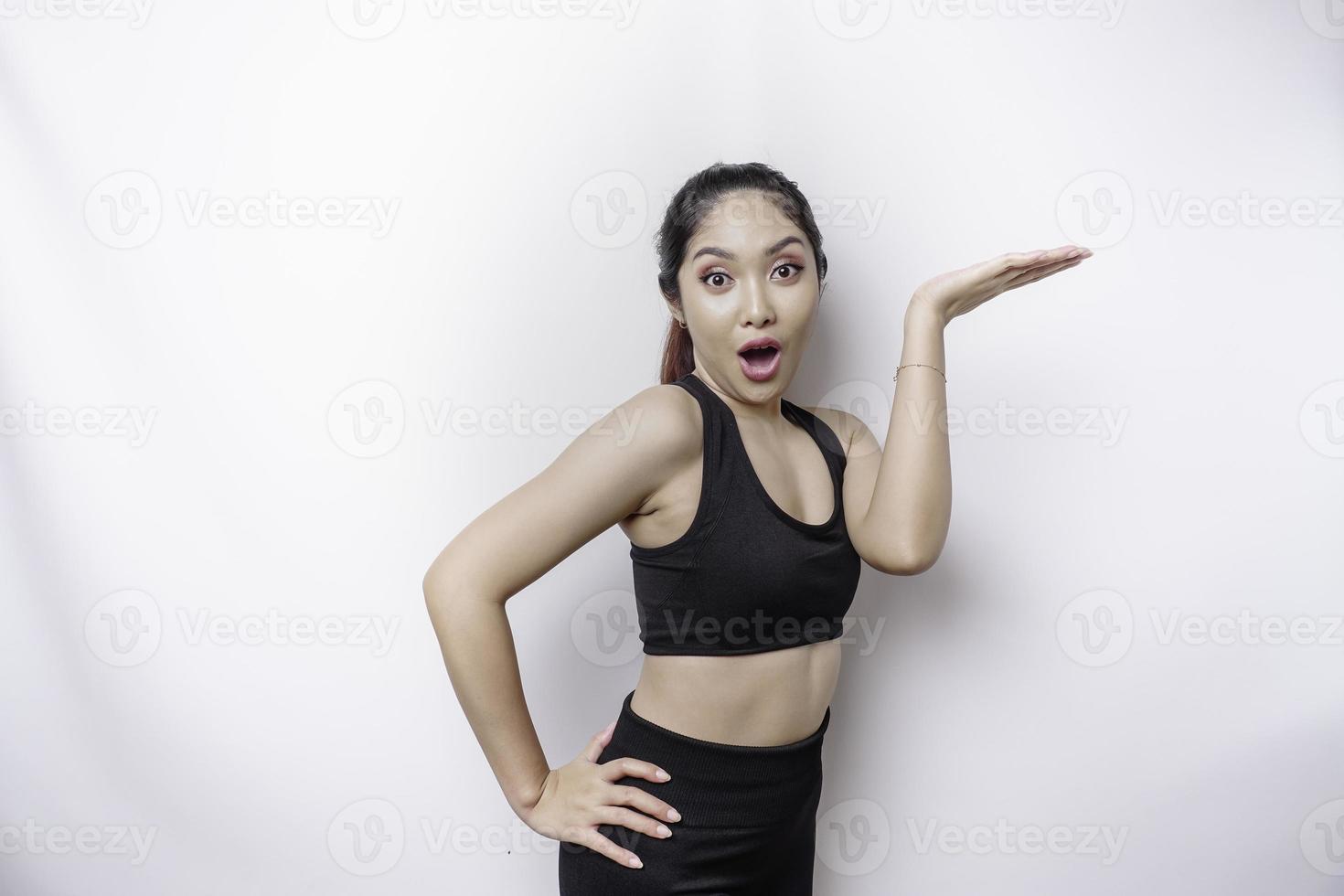 Shocked Asian sporty woman wearing sportswear pointing at the copy space on top of her, isolated by white background photo