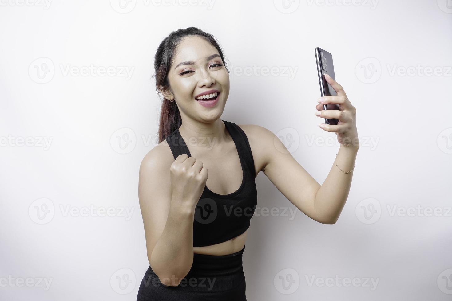 A young sporty Asian woman with a happy successful expression wearing sportswear and holding smartphone isolated by white background photo