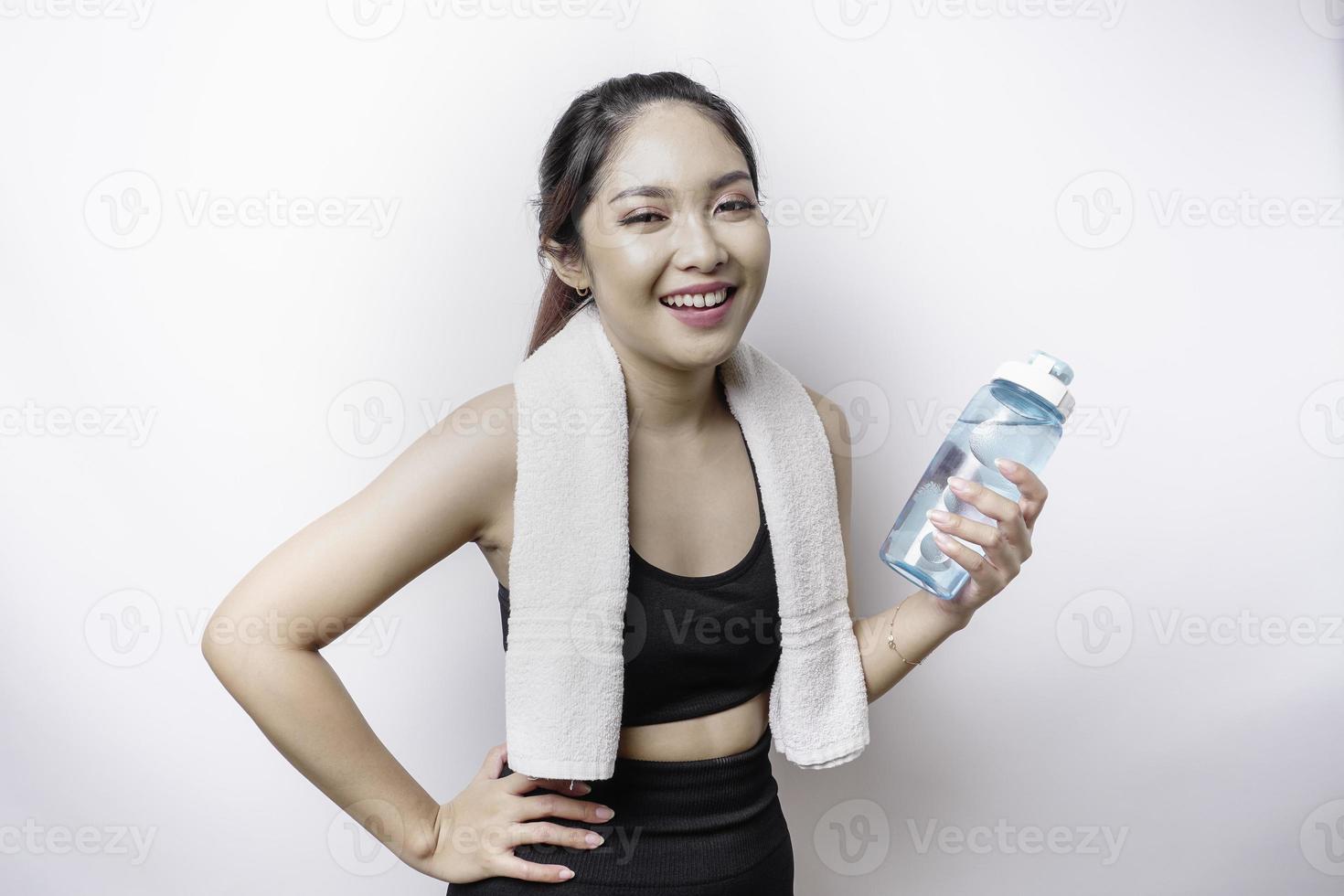 Sportive Asian woman posing with a towel on her shoulder and holding a bottle of water, smiling and relaxing after workout photo