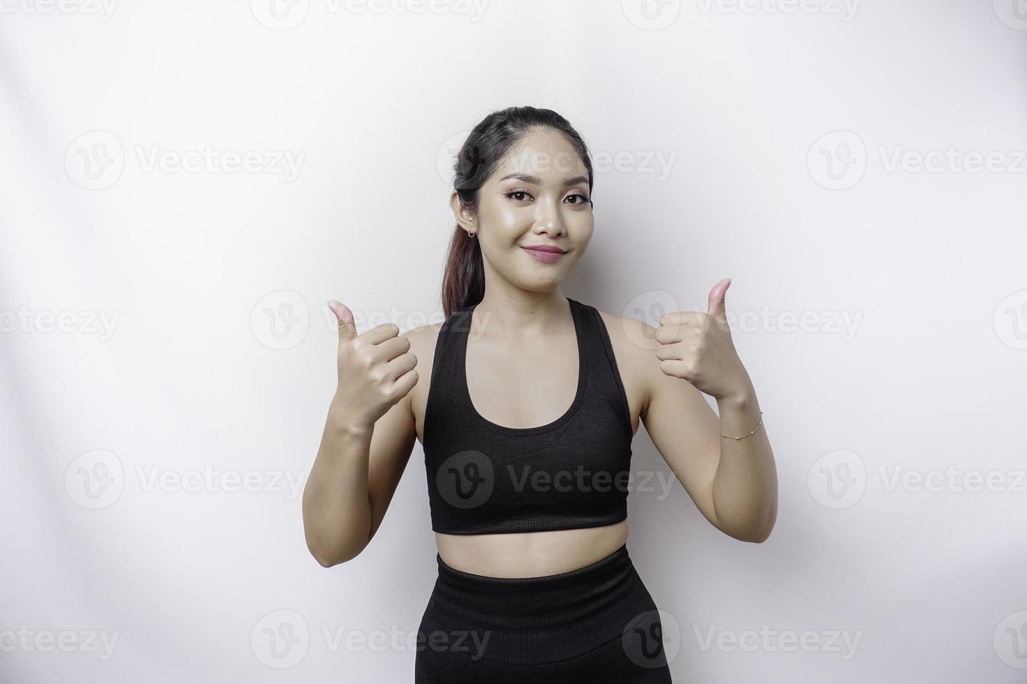 Excited sporty Asian woman wearing sportswear gives thumbs up hand gesture of approval, isolated by white background photo