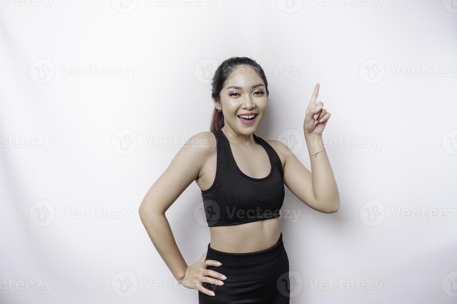 emocionada mujer deportiva asiática usando ropa deportiva apuntando al espacio de copia encima de ella, aislada por fondo blanco foto