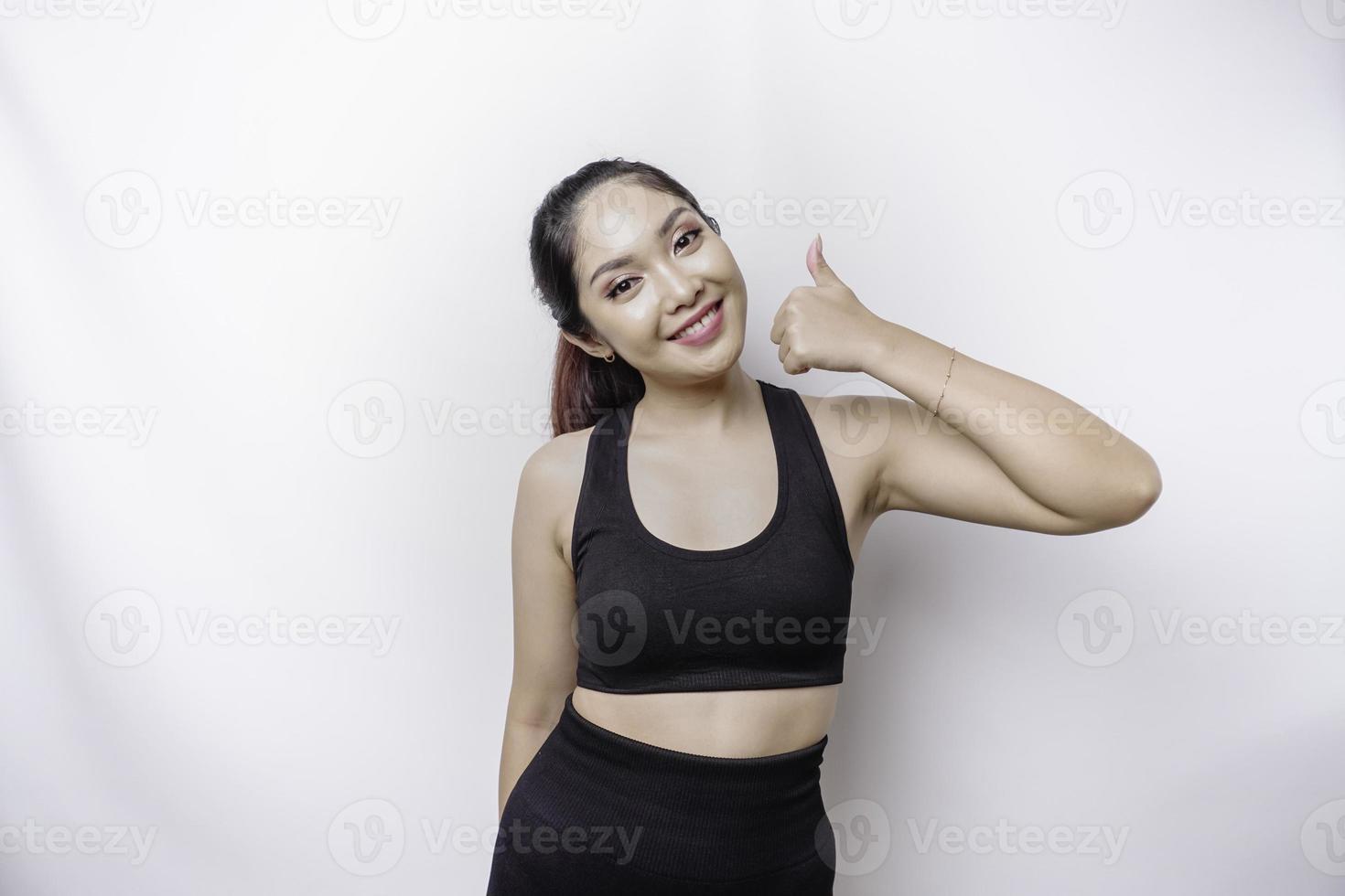 Excited sporty Asian woman wearing sportswear gives thumbs up hand gesture of approval, isolated by white background photo