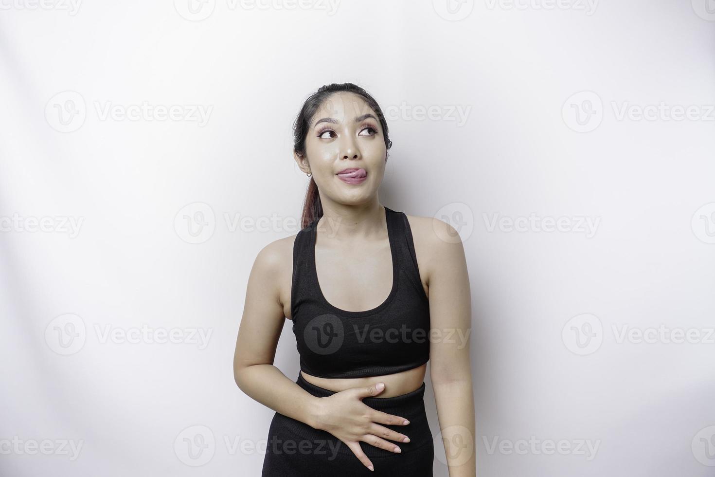 A sporty Asian woman is hungry and touching her belly while looking aside thinking what to eat photo