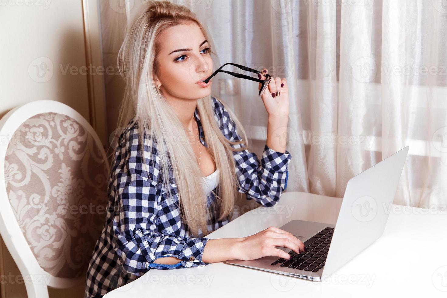 Beautiful blonde girl with blue eyes with laptop on desk looking away photo