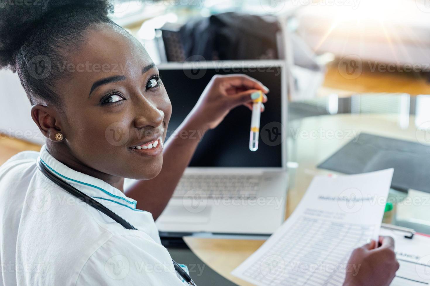 Female doctor in white coat holding blood test tubes in hands while wrapped up in work at modern lab. Female life science professional holding glass cuvette. Healthcare and biotechnology concept. photo