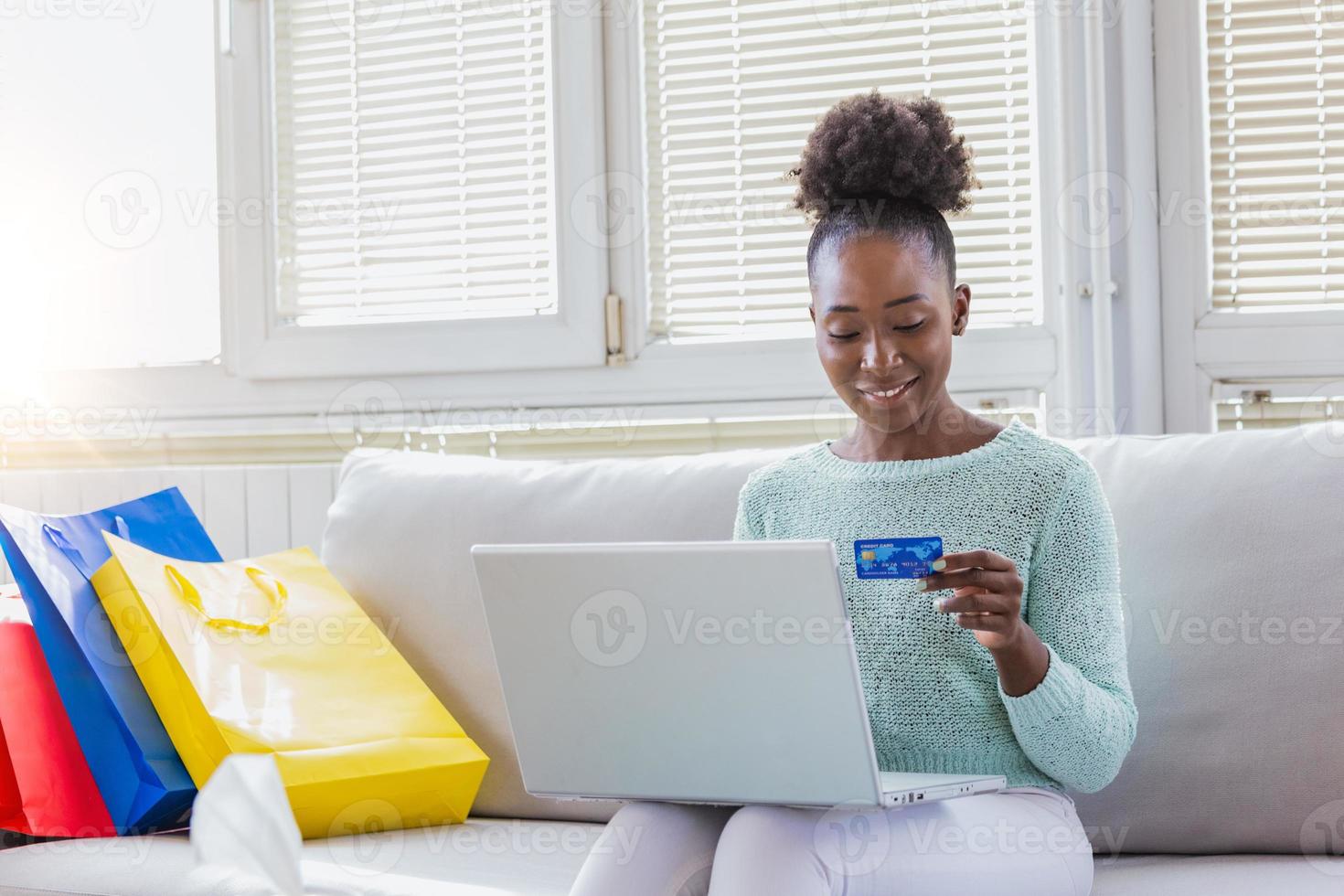 Young Woman On Sofa Shopping Online With Laptop. Young black woman inputting card information while shopping online. Online shopping concept photo