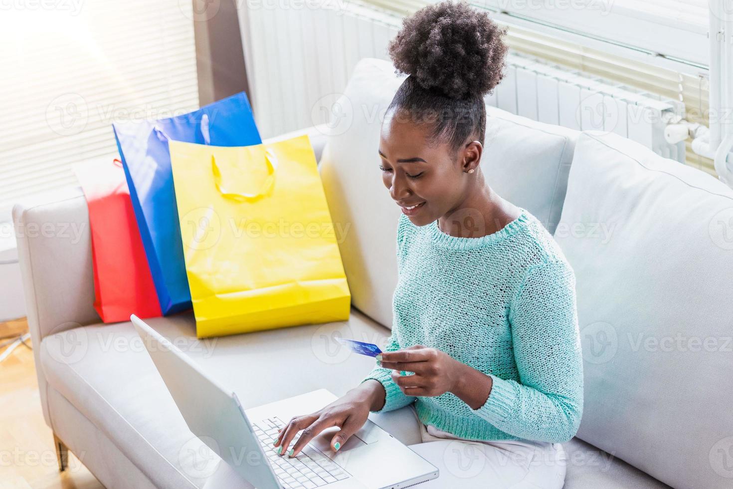 la mujer tiene una tarjeta de crédito y usa una computadora portátil. concepto de compras en línea. joven afroamericana está comprando artículos de moda con tarjeta de crédito foto